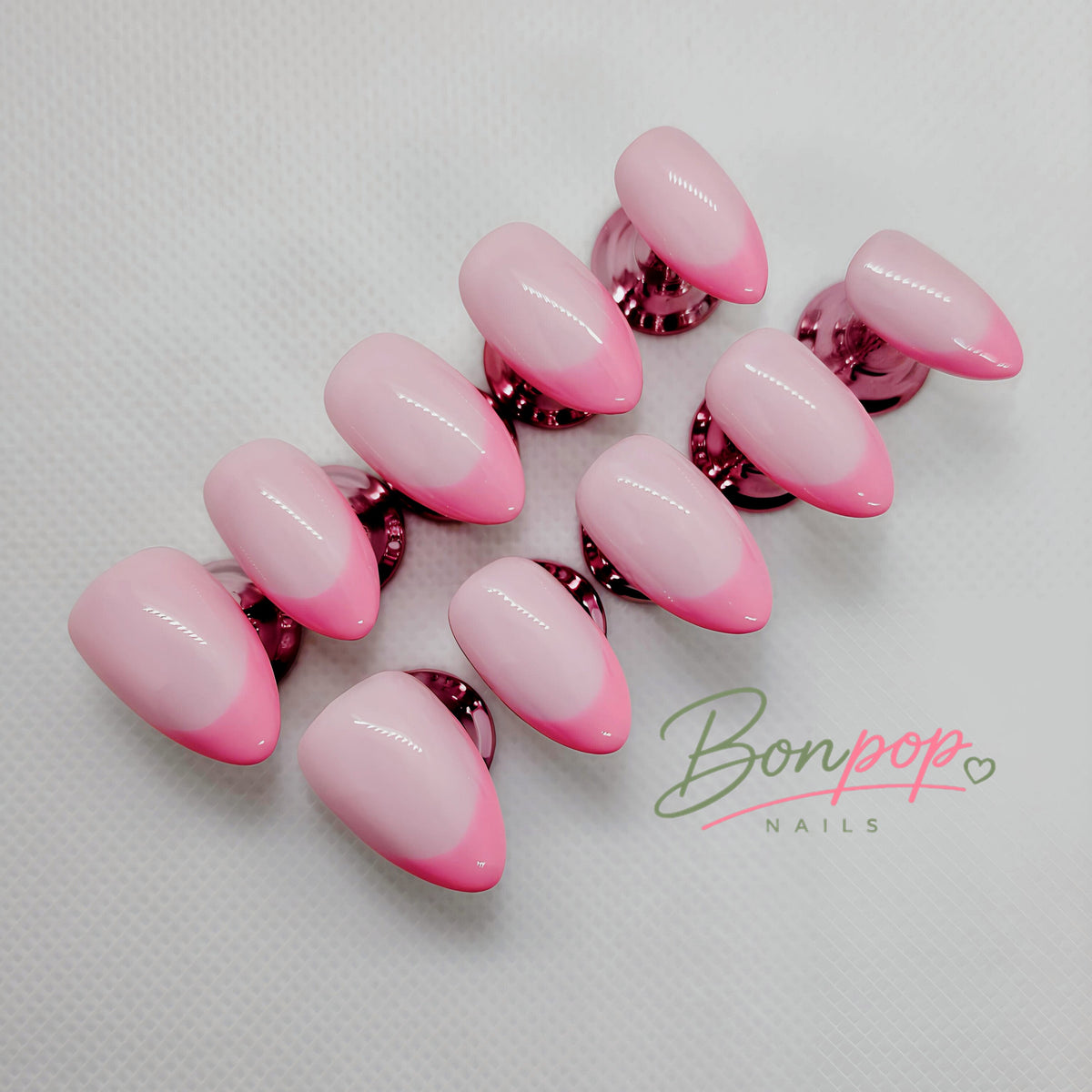 A set of artificial press-on nails with a glossy pink ombre gradient, transitioning from light pink to vibrant hot pink, displayed on a textured white background with a 'Bonpop Nails' logo watermark.