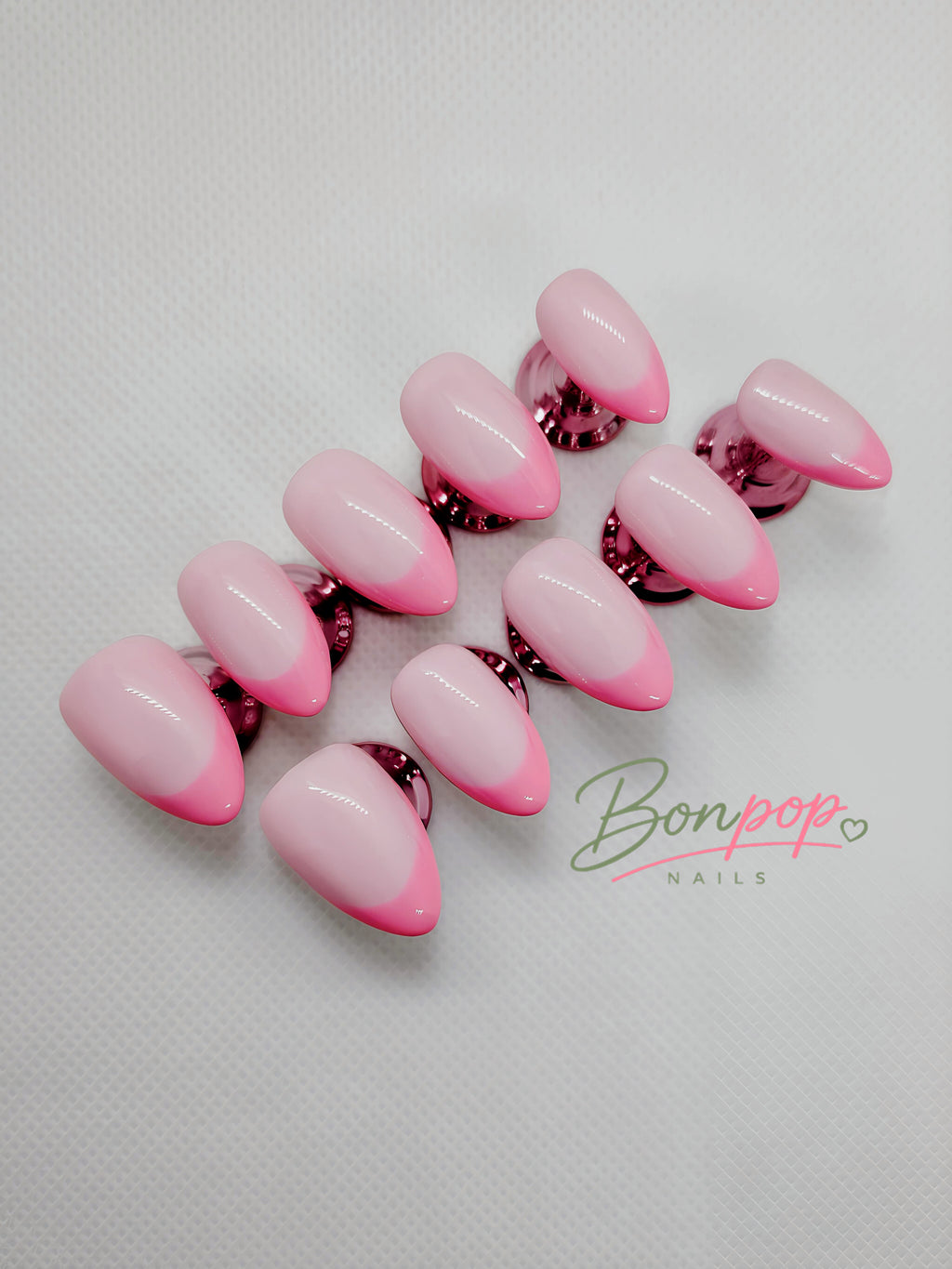A set of artificial press-on nails with a glossy pink ombre gradient, transitioning from light pink to vibrant hot pink, displayed on a textured white background with a 'Bonpop Nails' logo watermark.